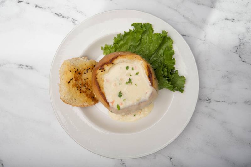 Clam chowder in a bread bowl, with a slice of toasted bread and a lettuce leaf