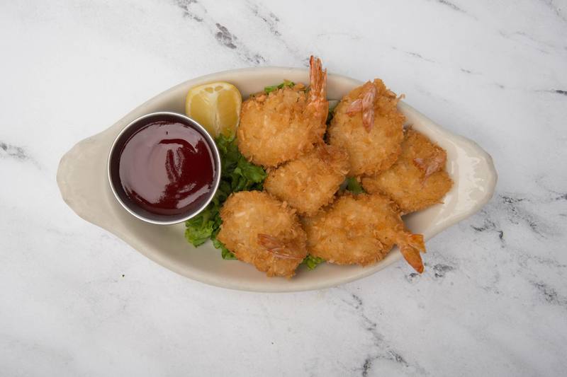 Coconut prawns on lettuce with a lemon wedge and a cup of sweet and sour sauce