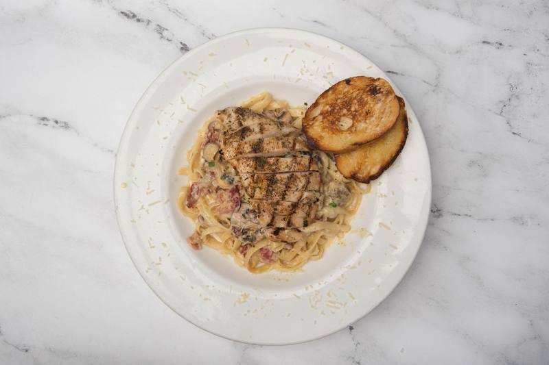 Fettuccine Alfredo with sliced grilled chicken, bacon and mushrooms, and two slices of garlic bread