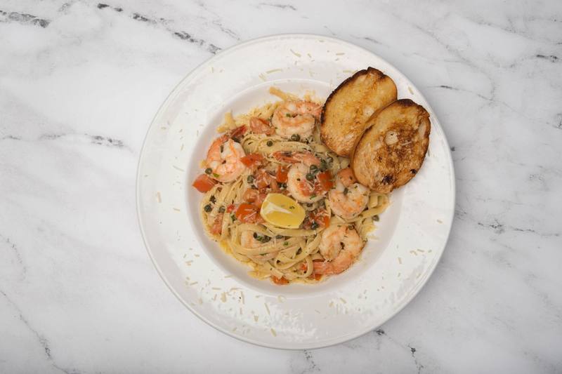 Prawn scampi over pasta with diced tomatoes and a lemon wedge, and two slices of garlic bread